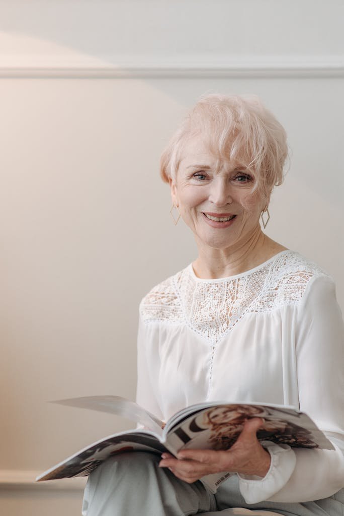Portrait of a smiling senior woman holding a magazine indoors against a light background.